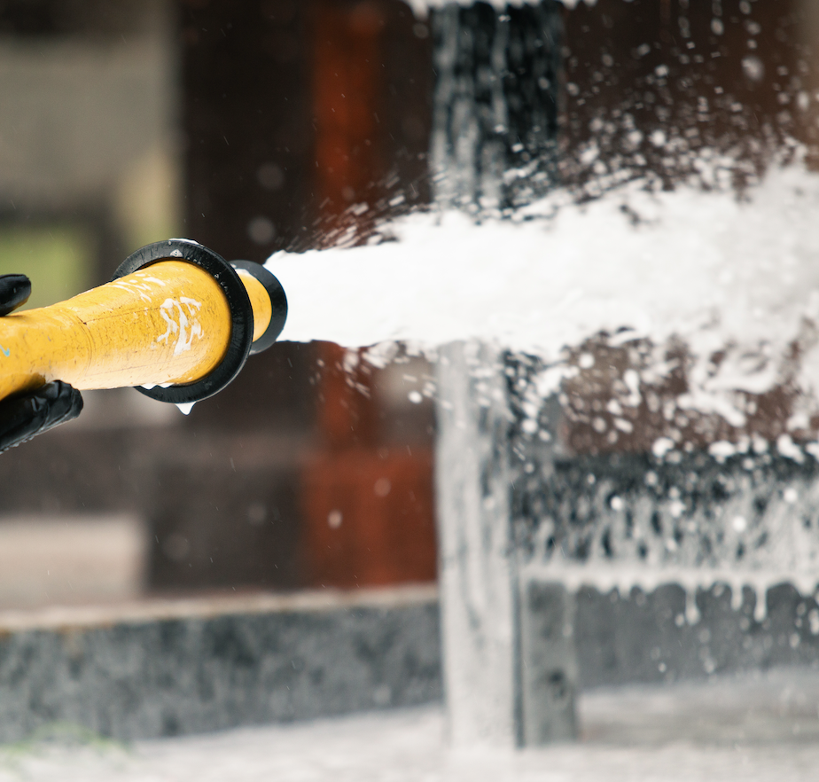 Firefighting foam sprayed from a yellow hose nozzle